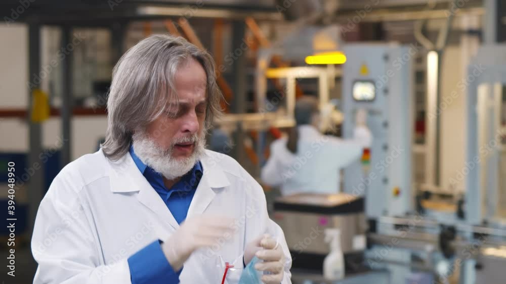 Sick mature chemist coughing and putting on medical mask at manufacturing plant Sick mature chemist coughing and putting on medical mask at manufacturing plant