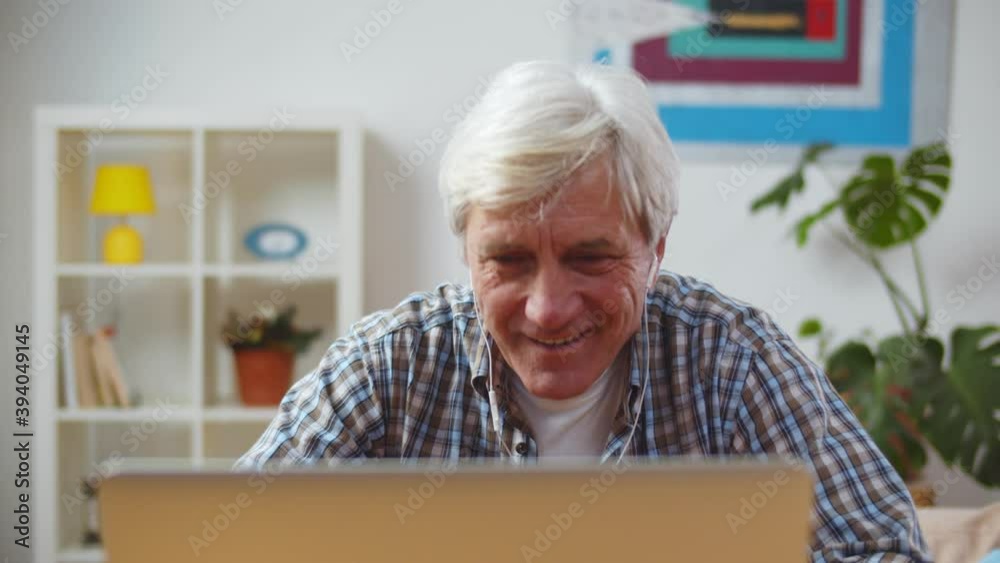 Portrait of handsome grey-haired man wearing headphones and listening to music on laptop Portrait of handsome grey-haired man wearing headphones and listening to music on laptop