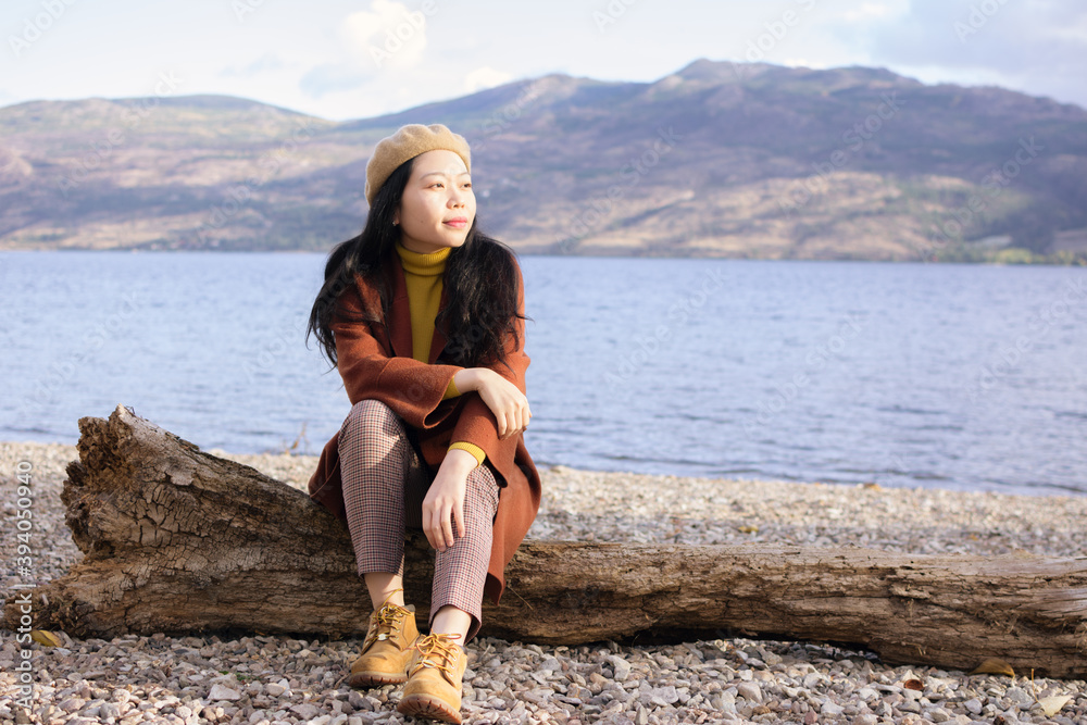 Young Asian Woman With Fall / Autumn / Spring Fashion Wear Sitting Down On A Log By A Lake