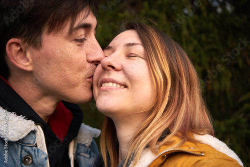 Enamored man kisses a smiling woman in a park.