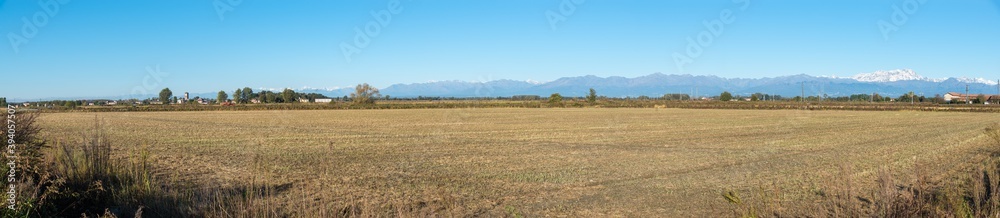 Fototapeta premium Fields in northern Italy with the Alpine chain in the background and on the left the town of San Nazzaro Sesia, province of Novara, Piedmont region. Panoramic view of the Po Valley 