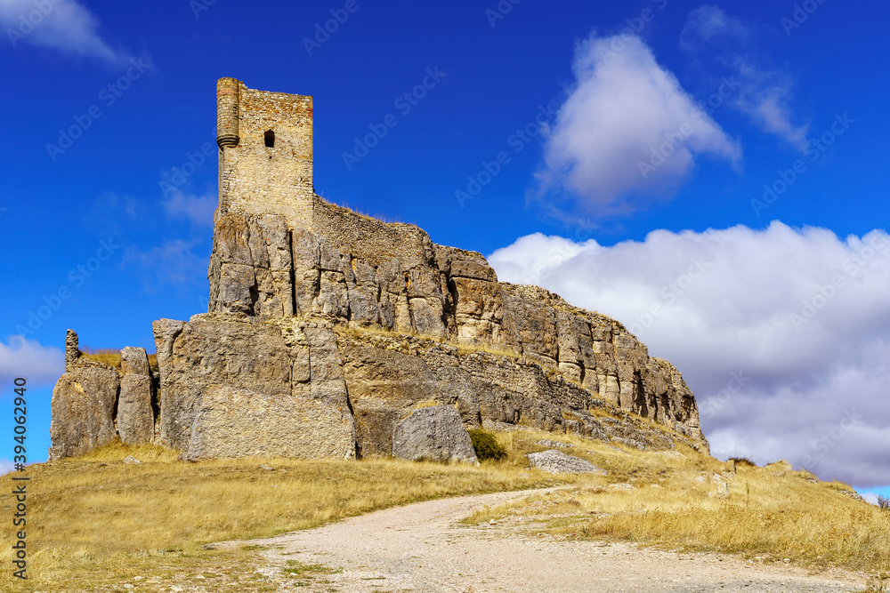 Castillo medieval de Atienza Guadalajara, alzándose en la colina con cielo azul y camino de tierra hacia el castillo.
