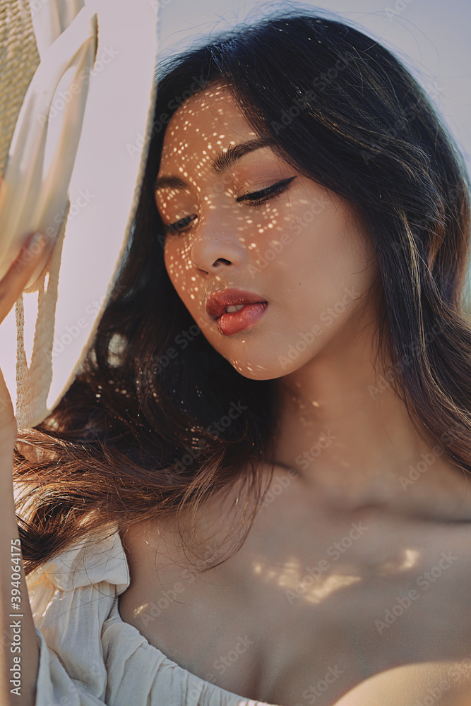 Lifestyle fashion portrait of stylish young asian woman with straw hat posing outdoor . Wearing straw hat and beige outfit .Summer bright colors.