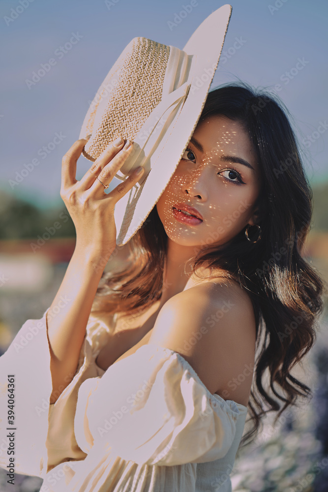 Lifestyle fashion portrait of stylish young asian woman with straw hat posing outdoor . Wearing straw hat and beige outfit .Summer bright colors.