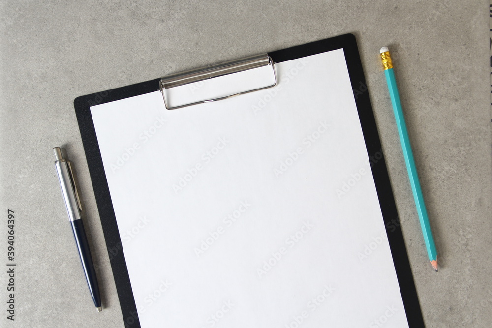 Template of white paper with a ballpoint pen and simple pencil on light grey concrete background in a black tablet with a clip. Concept of new idea, business plan and strategy, empty space for text Template of white paper with a ballpoint pen and simple pencil on light grey concrete background in a black tablet with a clip. Concept of new idea, business plan and strategy, empty space for text