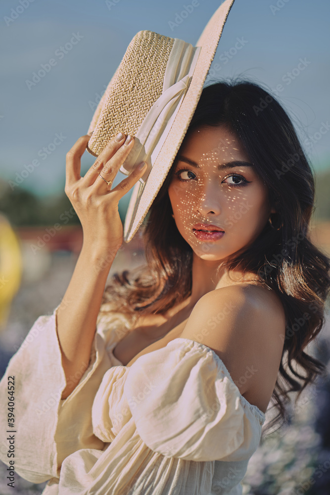 Lifestyle fashion portrait of stylish young asian woman with straw hat posing outdoor . Wearing straw hat and beige outfit .Summer bright colors.