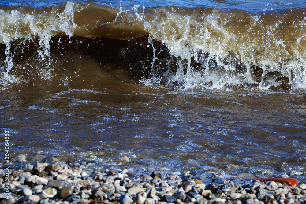waves run onto the shore and crash against the rocks, creating many splashes and splashes near the shore. river surf in stormy weather near a stone pebble coast with foamy splashing waves. waves run onto the shore and crash against the rocks, creating many splashes and splashes near the shore. river surf in stormy weather near a stone pebble coast with foamy splashing waves.
