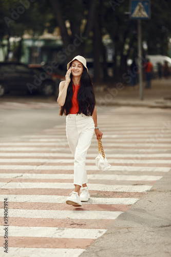 Portrait of beautiful brunette. Model in summer city. Woman walks with mobile phone.