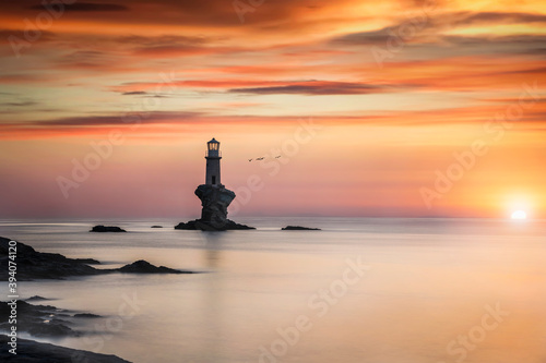 Romantic sunrise behind the famous Tourlitis lighthouse situated on a steep rock in the sea at the cycladic island of  Andros, Greece photo
