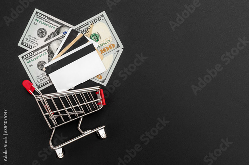 Credit cards, money and shopping cart on black. Top view. Copy space.