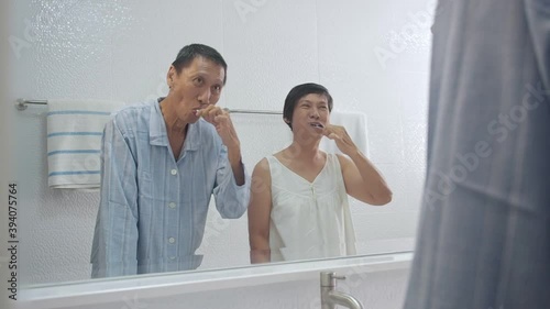 happy asian senior adult couple brushing teeth in clean white bathroom. Elderly grandmother and grandfather doing morning hygiene. grandparent playing while brushing teeth. looking into mirror.