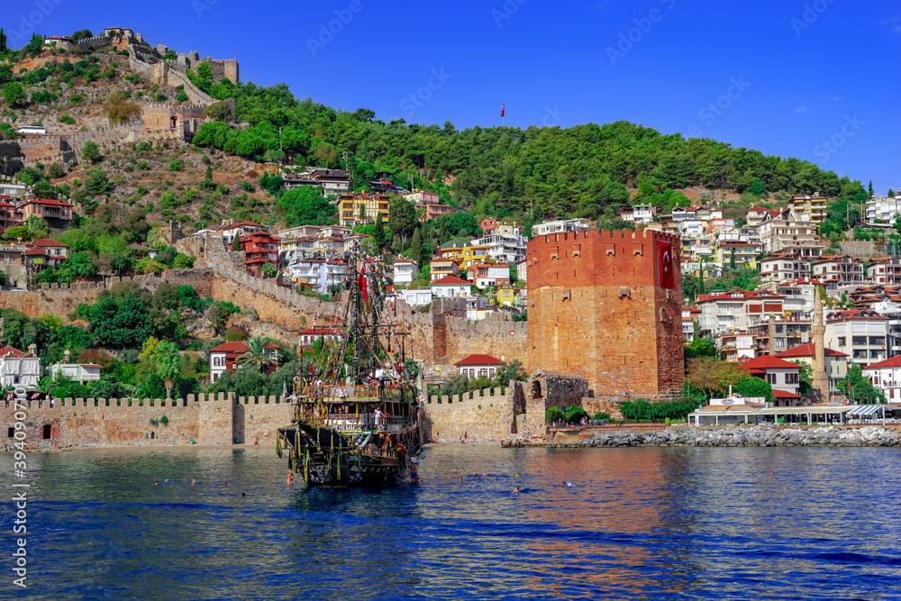 Turkey, Alanya - October 22, 2020: Tourist pirate ship near Kizil Kule tower in Alanya. Beautiful panorama of the Old Town of the Turkish resort - view from the Mediterranean Sea