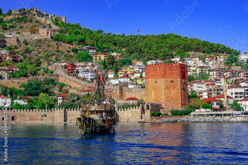 Turkey, Alanya - October 22, 2020: Tourist pirate ship near Kizil Kule tower in Alanya. Beautiful panorama of the Old Town of the Turkish resort - view from the Mediterranean Sea
