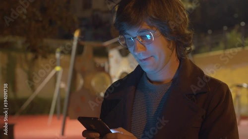 Smiling hipster typing in smartphone in the park near playground in the evening. Steadicam shot