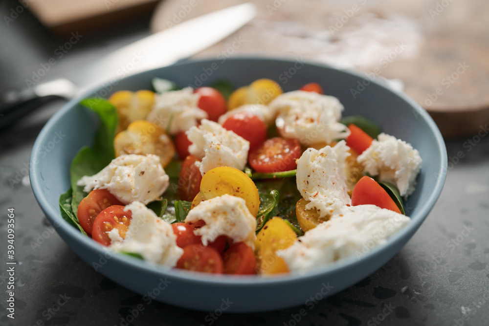 Salad with red and yellow cherry tomatoes , mozzarella and spinach in blue bowl on concrete countertop Salad with red and yellow cherry tomatoes , mozzarella and spinach in blue bowl on concrete countertop