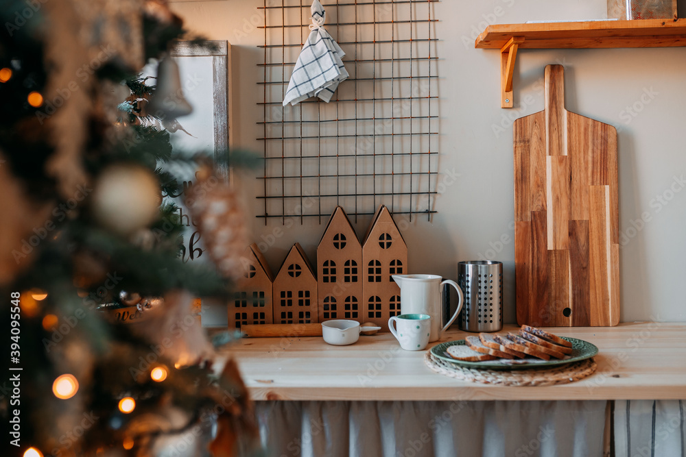 Scandinavian Christmas decorations. Little wooden houses with windows on the kitchen table. White tea cup and carafe. Festive table decorations.