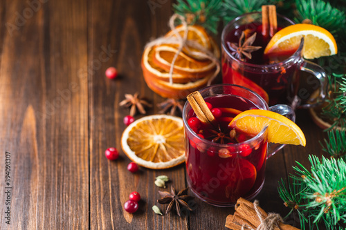 Hot wine drink with spices and fruits in a glass on a wooden background, branches of a Christmas tree and oranges, copy space. Christmas mulled wine or punch.