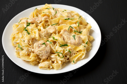 Homemade Chicken Fettuccine Alfredo on a white plate on a black background  side view. Copy space.