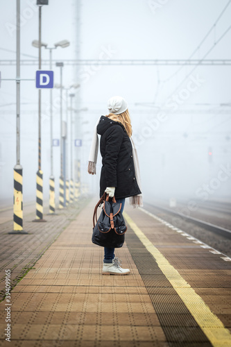 Woman with backpack waiting at railroad station for train. Foggy atmospheric mood in city
