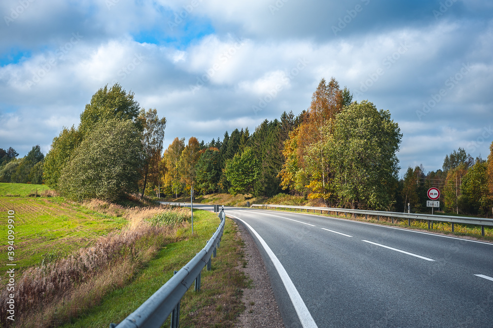 Fototapeta premium View of the highway road in the fall. Traveling background. Asphalt highway passing through the forest. Latvia. Baltic.