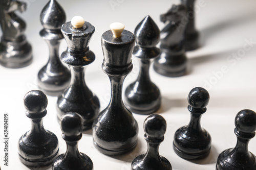 Wooden chess pieces. Black king Queen surrounded by her large retinue, full set of black side chess game, bright light from left, profile view