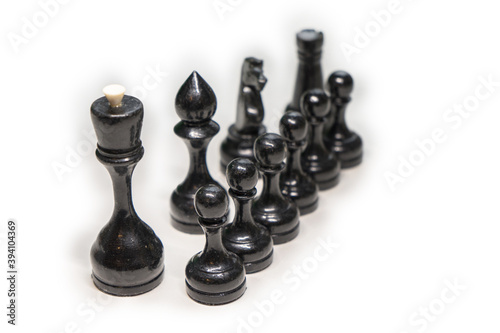 Wooden chess pieces. black pawns stand one after another, looking out from behind their comrades on a white background, focus on the second row of pawns, next to their main comrades, king, Bishop, kni