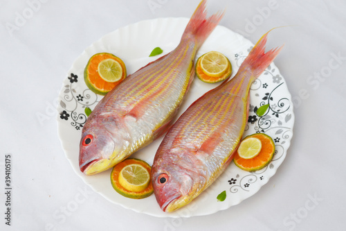 Close up view of fresh Pink Perch (thread finned Bream) Decorated with lemon slice,Orange slice and curry leaves on a white plate,White Background,Selective focus. photo