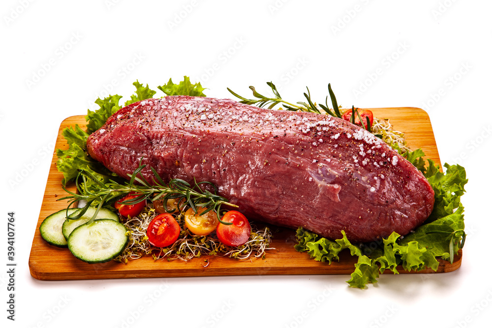 Fresh raw beef on cutting board with fresh vegetables on white background
Fresh raw beef on cutting board with fresh vegetables on white background