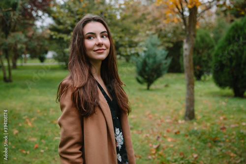 Portrait of young attractive woman in park. Woman in beige coat