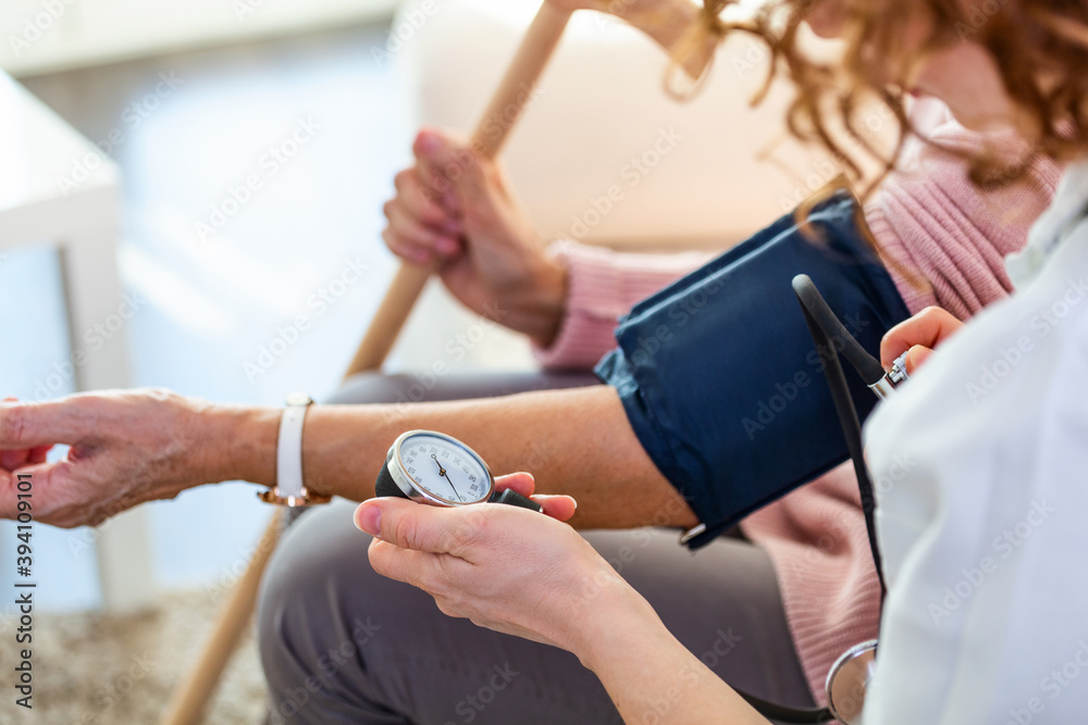 Obraz premium Nurse measuring blood pressure of senior woman at home. Smiling to each other. Young nurse measuring blood pressure of elderly woman at home. Doctor checking elderly woman's blood pressure