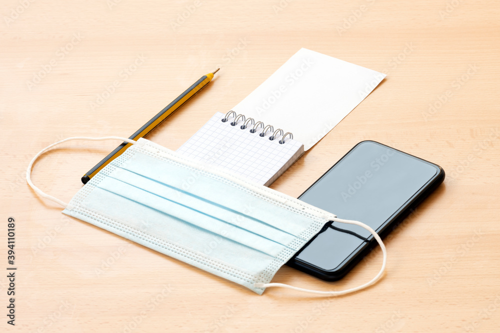 Flat lay with copy space, a face mask, a blank spiral notepad with a pen and a smart phone are arranged on a desk. To-do list concept during the Covid-19 outbreak. Flat lay with copy space, a face mask, a blank spiral notepad with a pen and a smart phone are arranged on a desk. To-do list concept during the Covid-19 outbreak.
