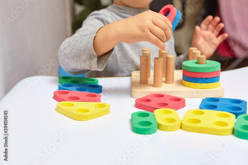 The child collects a sorter. Educational logic toys for kid's. Children's hands close-up. Montessori Games for Child Development. Multicolored logic sorter on white background.