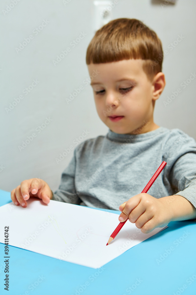 Cute little boy with blond hair draws colored pencils at home. Draws at the blue table. Cute little boy with blond hair draws colored pencils at home. Draws at the blue table.