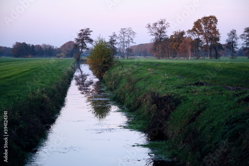 Dutch Frisian polder landscape scene with green pasture meadows, ditch, canal. Cold autumn evening, dusk. Netherlands, Ureterp photo