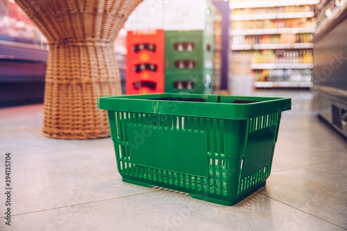 Green plastic shopping cart stands on the floor in the supermarket.