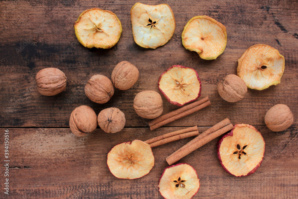 Dried fruits apples rings, walnuts, and cinnamon sticks on wooden background. Top view. Rustic style. Selective focus Dried fruits apples rings, walnuts, and cinnamon sticks on wooden background. Top view. Rustic style. Selective focus