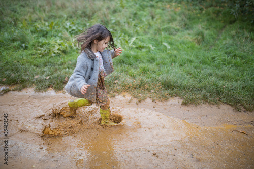 Happy little girl splashing and running through a muddy puddle photo