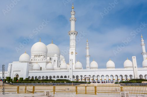 Panorama of White Grand Mosque with fence against blue sky, also called Sheikh Zayed Grand Mosque, inspired by Persian, Mughal and Moorish mosque architecture
