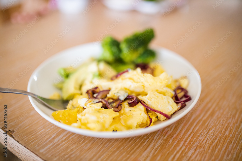 Broccoli and scrambled eggs with avocado slices on wooden table Broccoli and scrambled eggs with avocado slices on wooden table