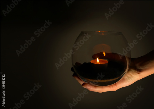 A burning candle in a glass ball is held by a hand