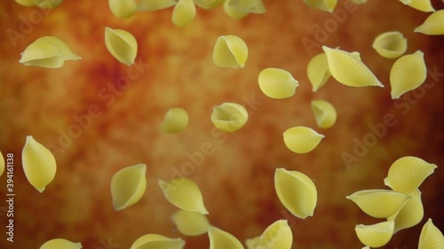 Dry pasta Conchiglie rigate is rotating on a yellow ochre background in slow motion photo