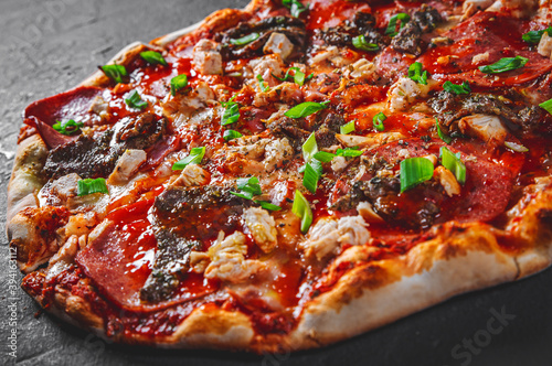 Pizza with Mozzarella cheese, salami, chicken meat, beef, ham, Tomato sauce, pepper, spices. Italian pizza on Dark grey black slate background