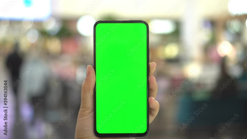 Shopping center. Department store. Mall. Back view of brunette holding chroma key green screen smartphone watching content. Shopping online. Gadgets and contemporary people concept. Shopping center. Department store. Mall. Back view of brunette holding chroma key green screen smartphone watching content. Shopping online. Gadgets and contemporary people concept.