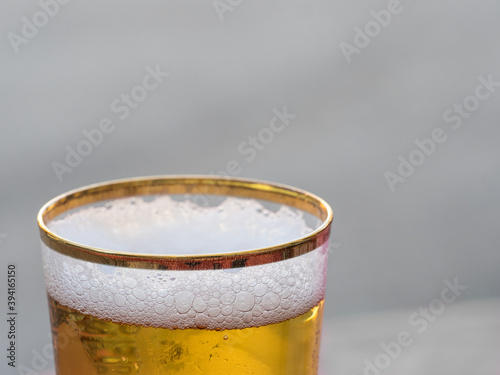 Close view of the froth in a newly poured gold rimmed glass of beer.Focus on front edge of glass deliberate blur to plain background.Drink