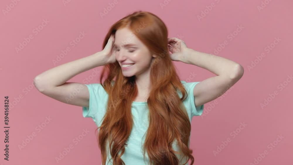 Smiling cheerful redhead young woman in casual blue turquoise t-shirt posing isolated on pastel pink background in studio. People lifestyle concept. Dancing clenching fists rising hands shaking head Smiling cheerful redhead young woman in casual blue turquoise t-shirt posing isolated on pastel pink background in studio. People lifestyle concept. Dancing clenching fists rising hands shaking head