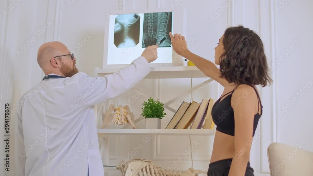 The Doctor Shows the Young Woman her X-ray, Evaluating the Patient's Condition in Order to Suggest Appropriate Treatment. Back Health The Doctor Shows the Young Woman her X-ray, Evaluating the Patient's Condition in Order to Suggest Appropriate Treatment. Back Health
