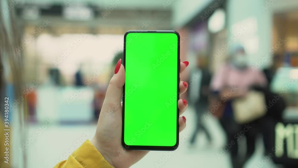 Shopping center. Department store. Mall. Back view of brunette holding chroma key green screen smartphone watching content. Shopping online. Gadgets and contemporary people concept. Shopping center. Department store. Mall. Back view of brunette holding chroma key green screen smartphone watching content. Shopping online. Gadgets and contemporary people concept.