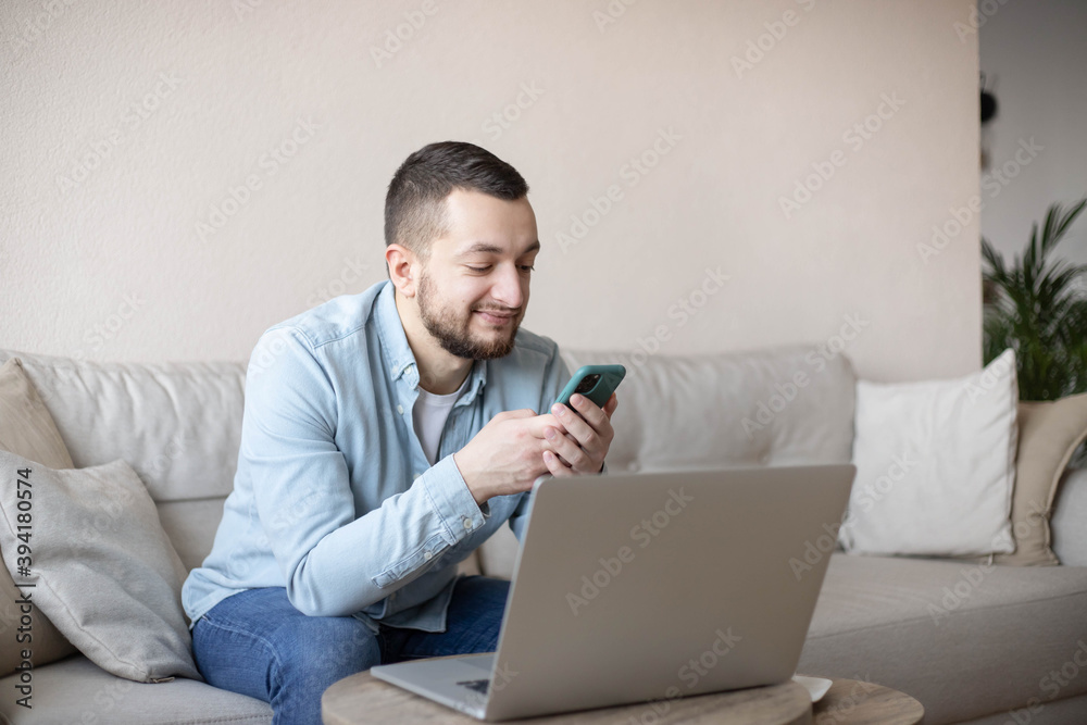 Businessman working at home using laptop and mobile phone. Home office. Young man sitting relaxed on sofa with laptop and smartphone. Businessman working at home using laptop and mobile phone. Home office. Young man sitting relaxed on sofa with laptop and smartphone.