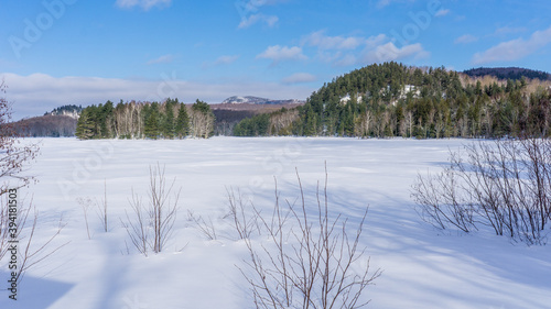 Hiking the forest of Mont Orford National Park in Quebec during winter. View of a lake during winter, covered in snow photo