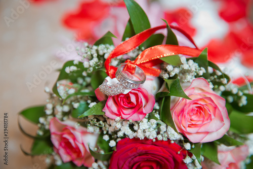 Rings on the wedding bouquet . The engagement rings are tied with ribbon Selective focus and blurred background . Gold wedding rings on a bouquet of red and white flowers.